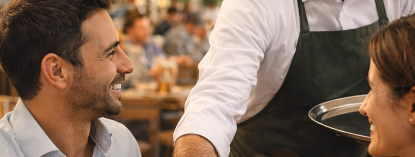 Ein Kellner serviert einem Gast im Restaurant einen Espresso und schafft damit eine typische Zusatzverkaufssituation in der Gastronomie.
