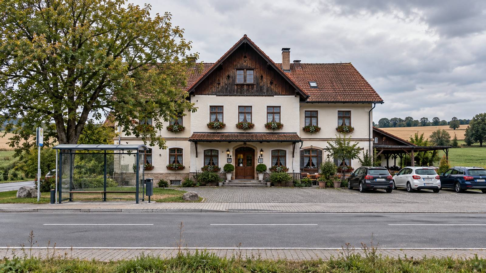 Alter Landgasthof an einer Dorfstraße mit Bushaltestelle und Parkplatz vor Feldern